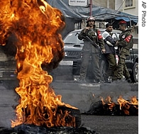 Palestinian police officers stand near burning tires blocking a road during a protest against the shooting deaths of three young sons of a senior intelligence office, in Gaza City early Monday, 12 Dec 2006